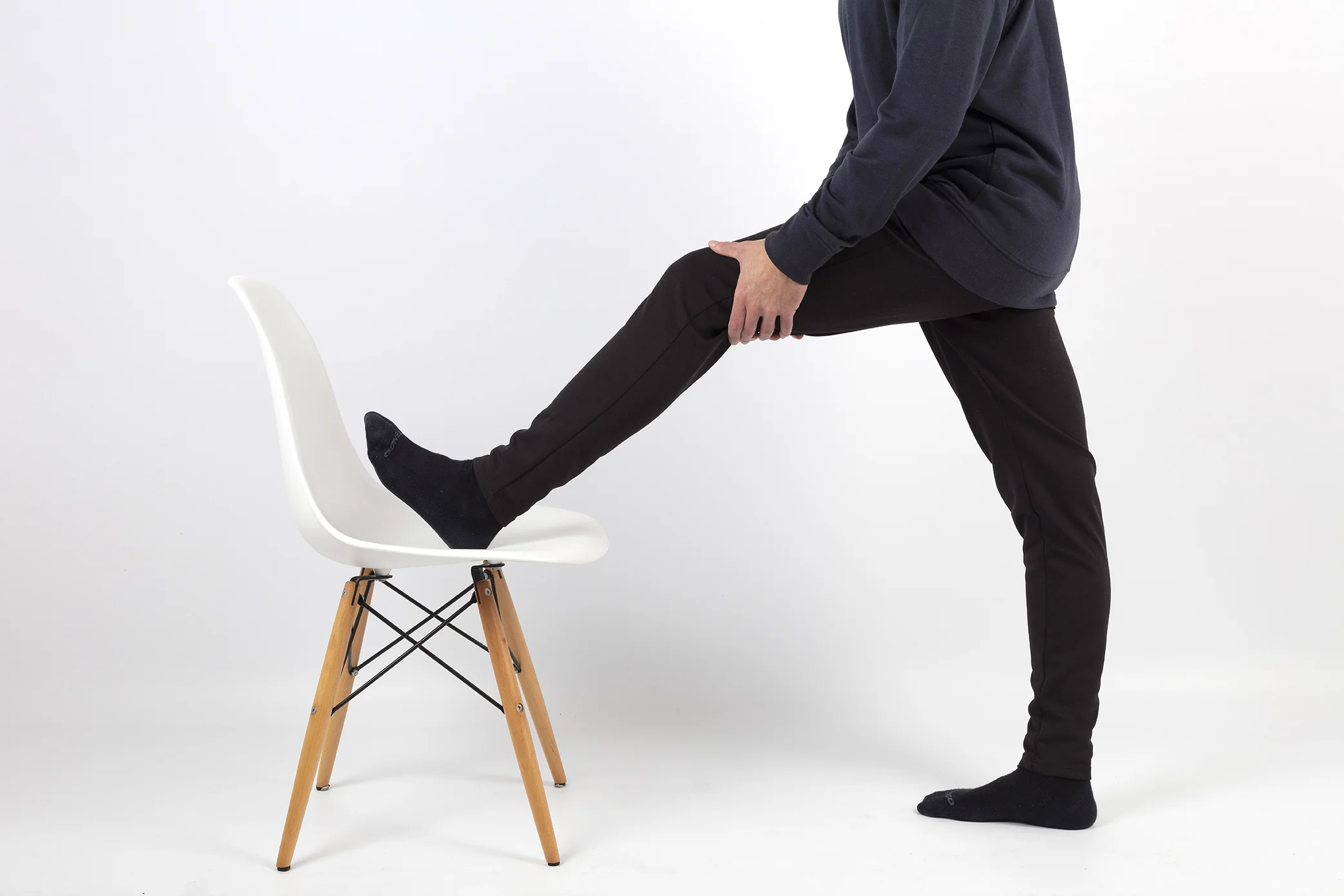 Fisioterapeuta realiza un estiramiento de la musculatura posterior de la pierna. Tiene el pie apoyado sobre una silla de color blanco que se encuentra en su casa.